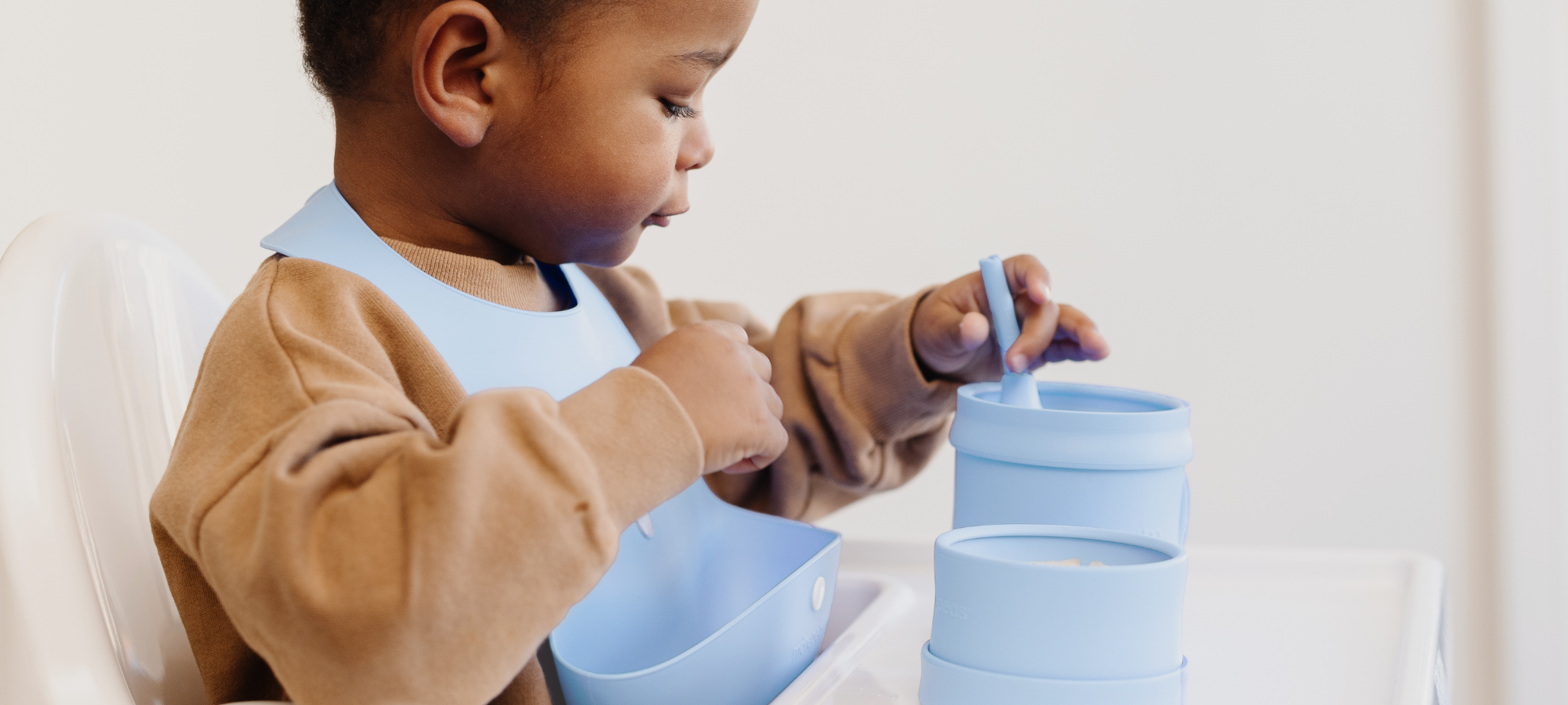 little boy at highchair wearing a morepeas bib and using morepeas tableware