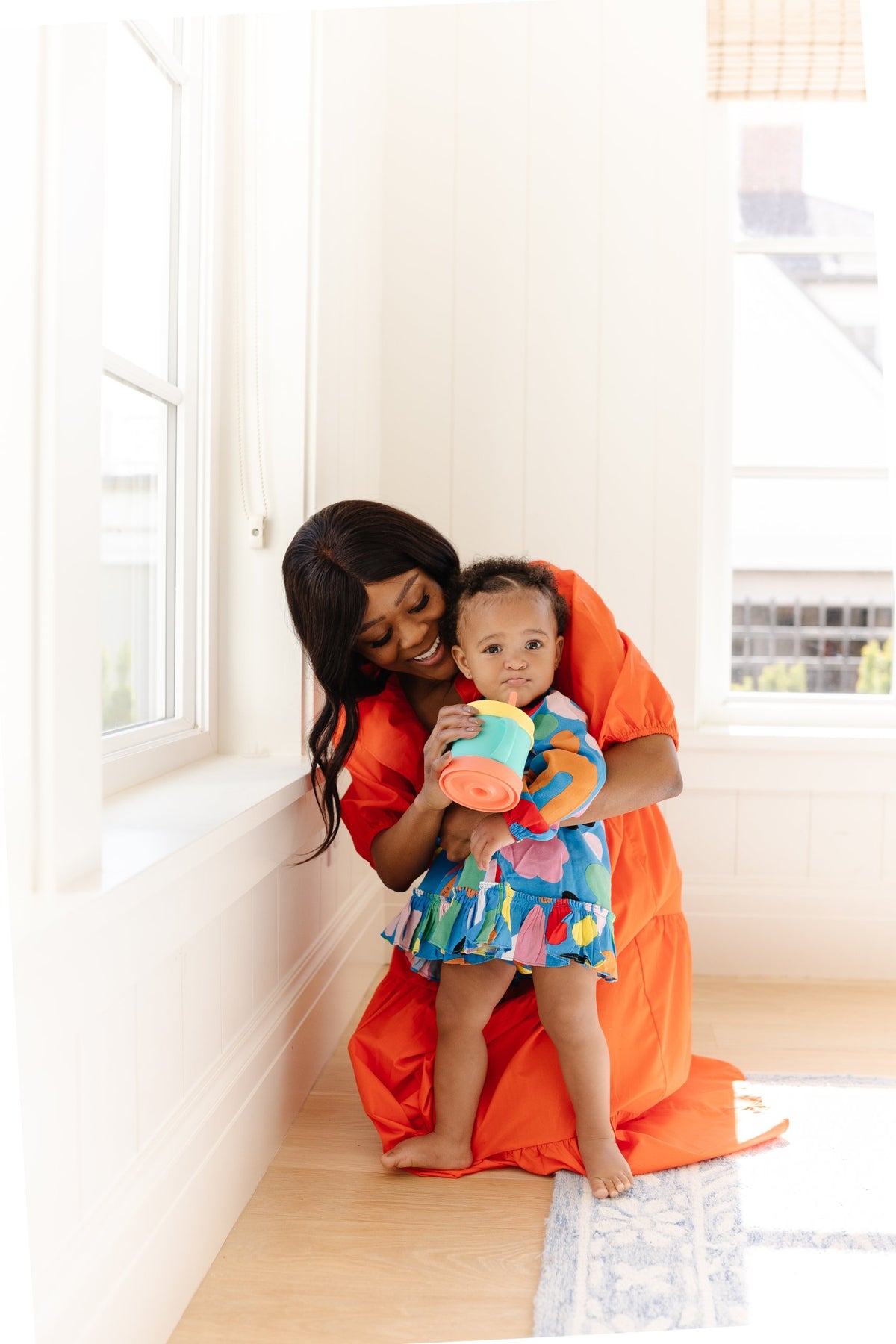 Mom in an orange dress kneeling with her toddler daughter, who holds a Morepeas snack cup