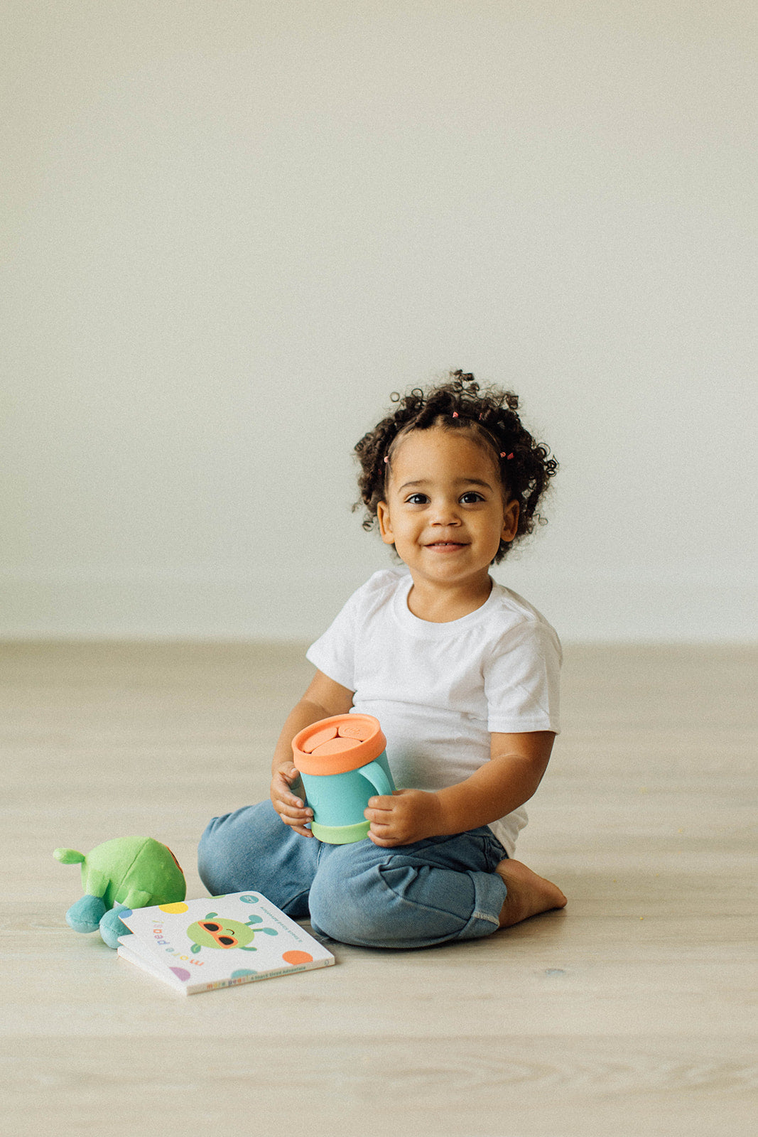 Toddler holding a Morepeas Snack Cup next to the Morepeas book and Percy the Pea plush