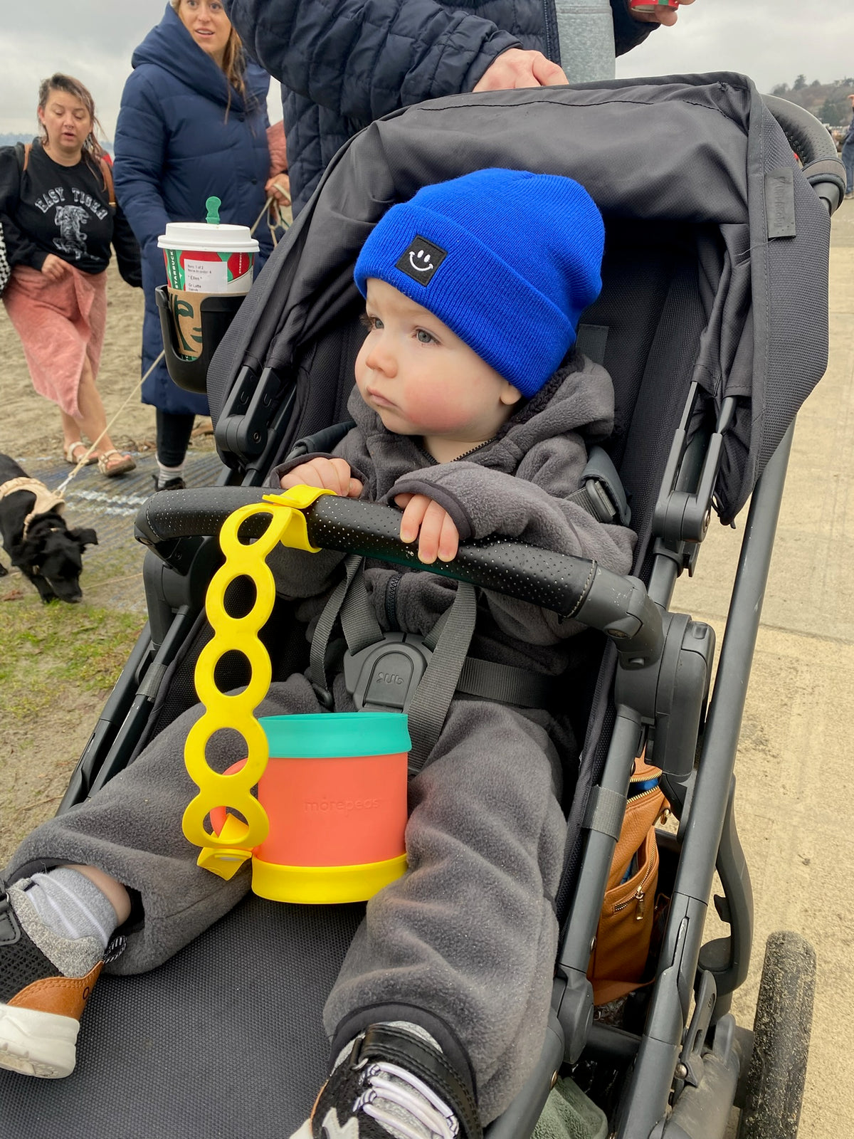 Toddler in a stroller with a Morepeas Snack Cup tethered to the bar with the On-the-Go Tether