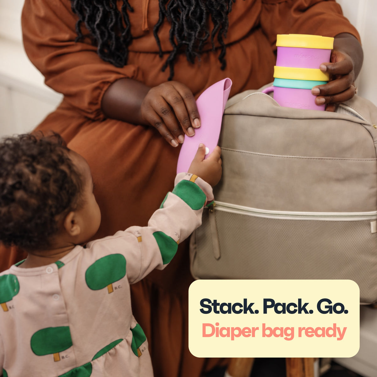 Toddler helping pack a Roll & Snap Bib and stacked Morepeas set into a diaper bag
