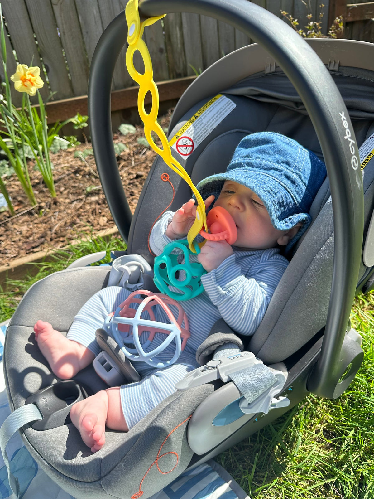 Baby in a car seat with a Morepeas pacifier and Wander Ball teether attached by the On-the-Go Tether
